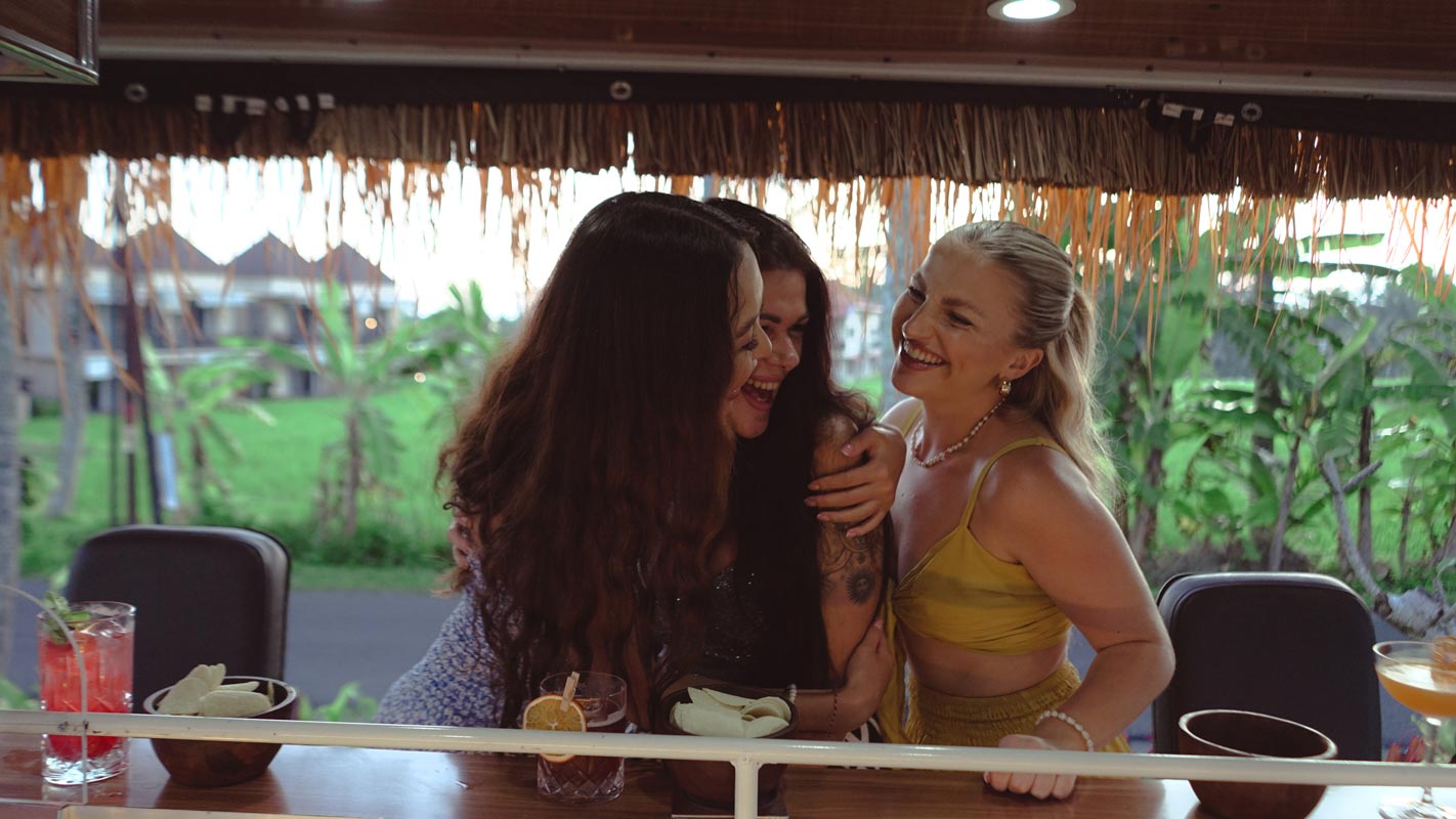 Friends laughing together at the Tikibus bar counter under the palm-thatched roof